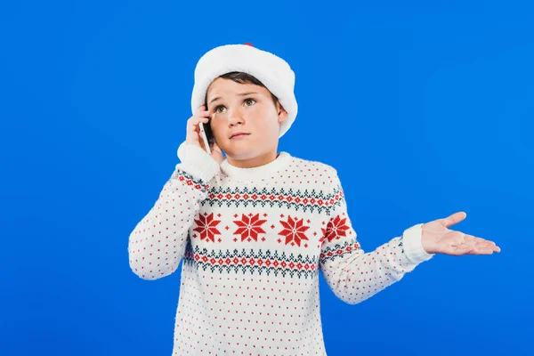 Confused kid in sweater talking on smartphone isolated on blue — Stock Photo