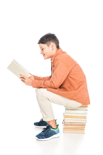 Улыбающийся ребенок сидит на книгах и читает на белом — стоковое фото