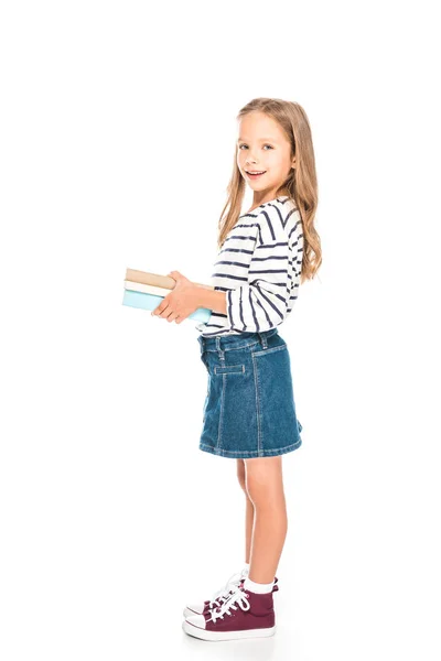 Vista completa de niño sonriente en falda de mezclilla sosteniendo libros aislados en blanco - foto de stock