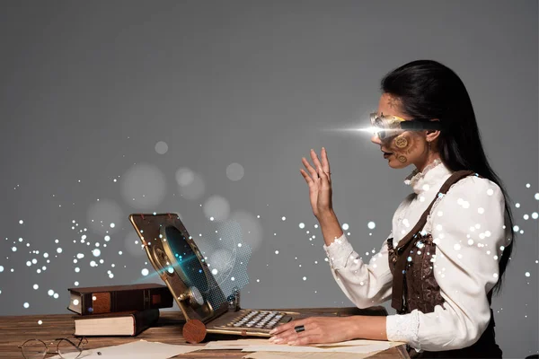 Steampunk woman in goggles waving hand during video chat with glowing digital illustration isolated on grey — Stock Photo