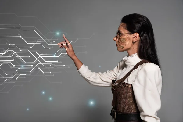 Cropped view of steampunk young woman in white blouse pointing with finger at glowing cyber illustration on grey — Stock Photo