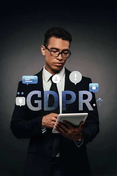 African american businessman in glasses using digital tablet on dark background with gdpr illustration — Stock Photo