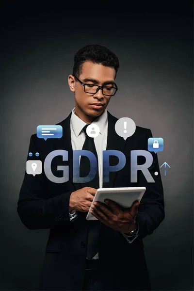 Hombre de negocios afroamericano en gafas usando tableta digital sobre fondo oscuro con ilustración gdpr - foto de stock