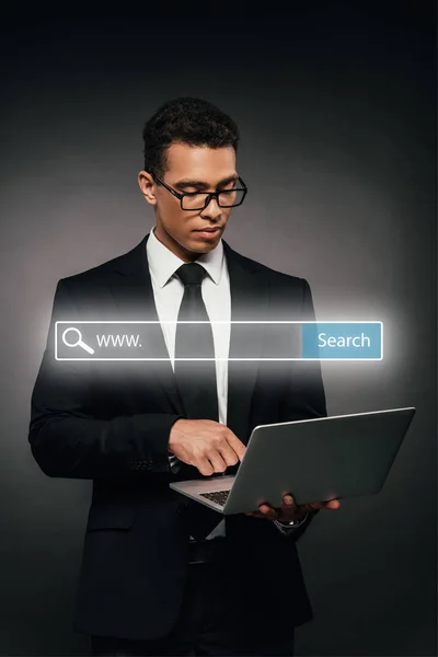 African american businessman using laptop on dark background with search bar illustration — Stock Photo