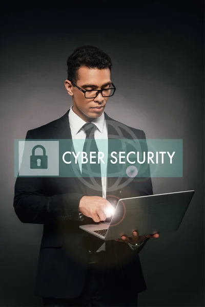 Hombre de negocios afroamericano utilizando portátil sobre fondo oscuro con ilustración de seguridad cibernética - foto de stock