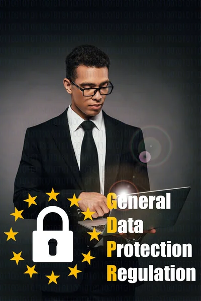 Hombre de negocios afroamericano utilizando portátil sobre fondo oscuro con ilustración gdpr - foto de stock