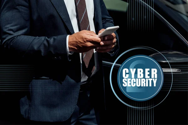 Cropped view of african american businessman in suit using smartphone at sunny day near car with cyber security illustration — Stock Photo