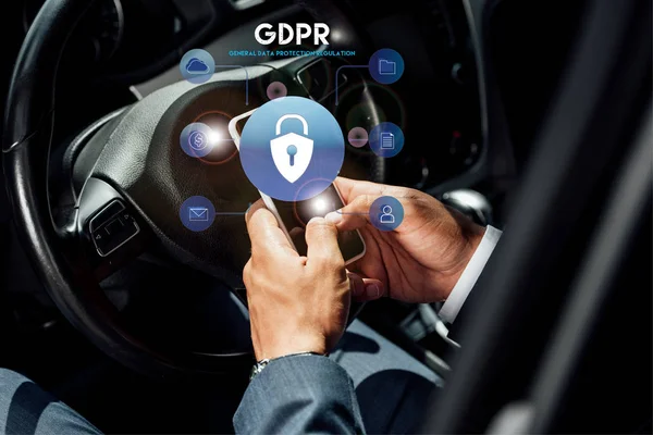 Partial view of african american businessman in suit using smartphone with gdpr illustration in car at sunny day — Stock Photo