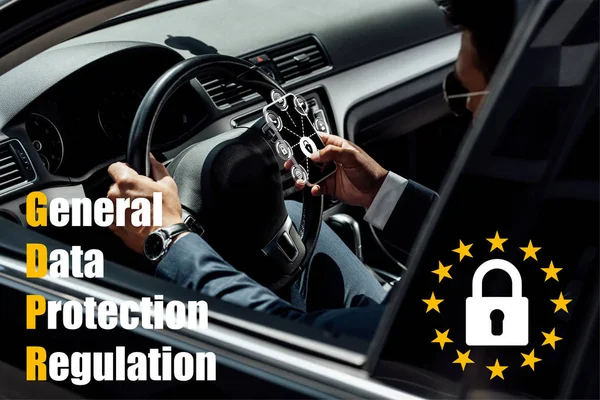 African american businessman in suit and sunglasses driving car and using smartphone with gdpr illustration — Stock Photo