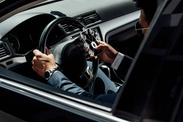 Afrikanischer amerikanischer Geschäftsmann in Anzug und Sonnenbrille, der Auto fährt und Smartphone mit Internet-Sicherheitssymbolen benutzt — Stockfoto