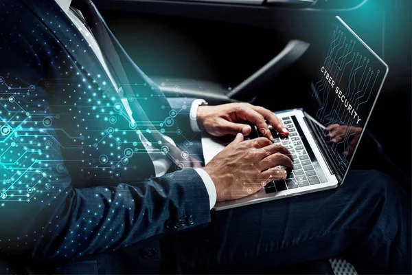 Vue partielle d'un homme d'affaires afro-américain utilisant un ordinateur portable avec une illustration de cybersécurité dans une voiture — Photo de stock