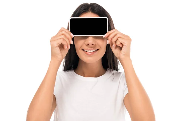 Mujer feliz cubriendo los ojos mientras sostiene el teléfono inteligente con pantalla en blanco aislado en blanco - foto de stock