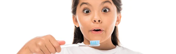 Plano panorámico del niño sorprendido mirando a la cámara y sosteniendo cepillo de dientes aislado en blanco - foto de stock