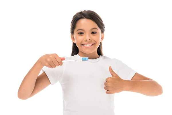 Счастливый ребенок, держащий зубную щетку и показывающий большой палец на белом — стоковое фото