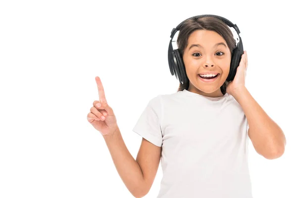 Happy kid listening music in headphones and pointing with finger isolated on white — Stock Photo