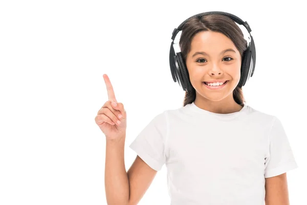 Adorable niño escuchando música en auriculares y señalando con el dedo aislado en blanco - foto de stock