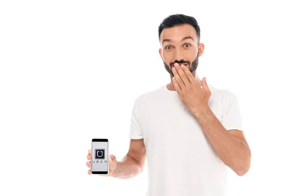 KYIV, UKRAINE - SETEMBRO 3, 2019: homem surpreso cobrindo boca e segurando smartphone com aplicativo uber na tela isolado no branco — Fotografia de Stock