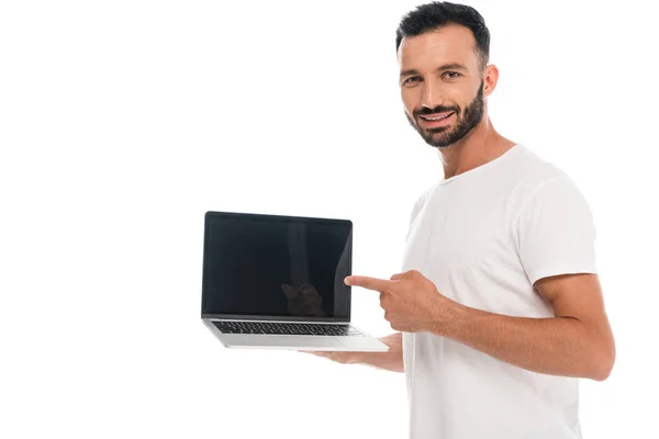 Hombre barbudo feliz apuntando con el dedo a la computadora portátil con pantalla en blanco aislado en blanco - foto de stock