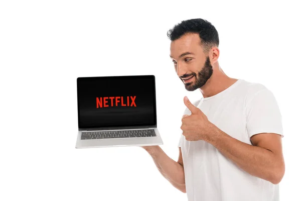 KYIV, UKRAINE - SEPTEMBER 3, 2019: happy bearded man showing thumb up and looking at laptop with netflix website on screen isolated on white — Stock Photo