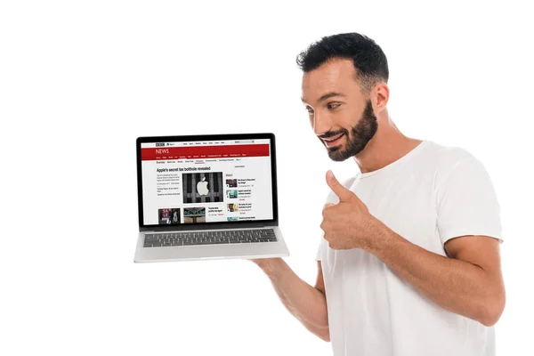 Київ, Україна - 3 вересня 2019: щасливий бородатий чоловік, що показує великий палець вгору і дивиться на ноутбук з bbc новинним сайтом на екрані ізольованим на білому — стокове фото