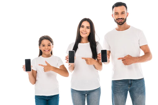 Счастливые родители и ребенок указывая пальцами на смартфоны с пустыми экранами изолированы на белом — стоковое фото