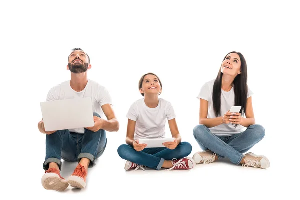 Allegra famiglia seduta con gadget e guardando in alto isolato su bianco — Foto stock