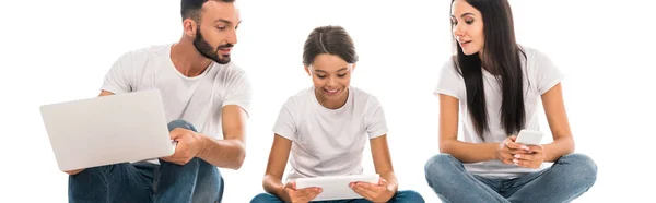 Панорамный снимок родителей, смотрящих на дочь с помощью устройства, изолированного на белом — стоковое фото
