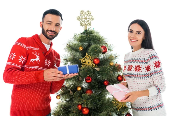 Alegre hombre y mujer sosteniendo regalos cerca de árbol de Navidad aislado en blanco - foto de stock