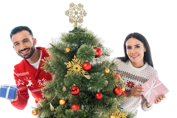 Feliz hombre y mujer sosteniendo regalos cerca de árbol de Navidad aislado en blanco - foto de stock