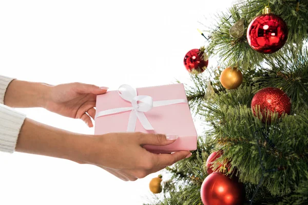 Vista recortada de la mujer sosteniendo presente cerca del árbol de Navidad aislado en blanco - foto de stock