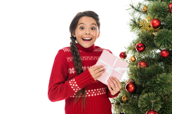 Niño emocionado sosteniendo regalo rosa cerca del árbol de Navidad aislado en blanco - foto de stock