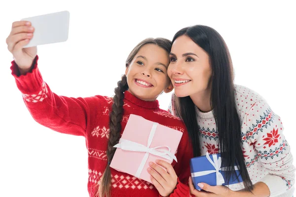 Feliz madre e hija en suéteres tomando selfie con presente aislado en blanco - foto de stock