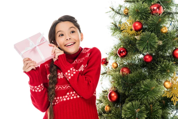 Cheerful kid in sweater holding gift near christmas tree isolated on white — Stock Photo