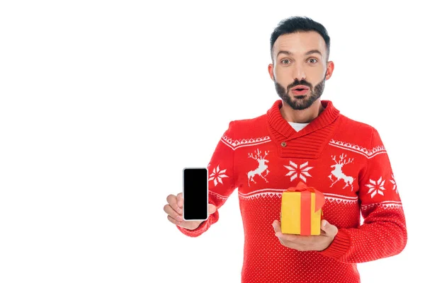 Здивований і бородатий чоловік тримає смартфон з порожнім екраном і подарунком ізольований на білому — стокове фото