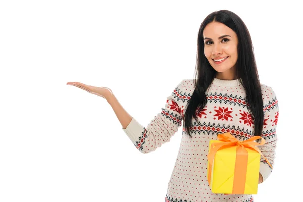 Fröhliche Frau im Pullover hält Geschenkschachtel in der Hand und zeigt mit der Hand isoliert auf weiß — Stockfoto