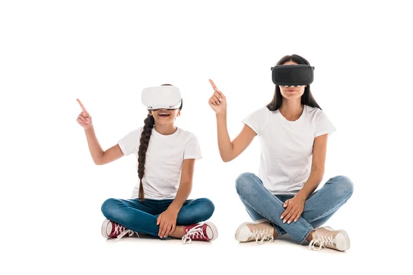 Mother and daughter using virtual reality headsets and pointing with fingers isolated on white — Stock Photo