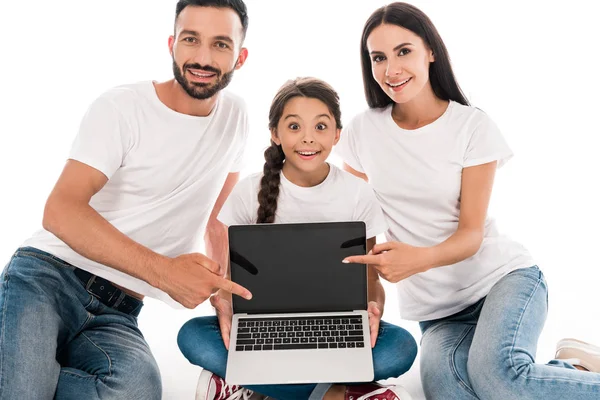 Happy parents in white t-shirts pointing with fingers at laptop with blank screen near daughter isolated on white — Stock Photo