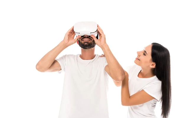 Mujer feliz mirando al hombre barbudo usando auriculares de realidad virtual aislados en blanco - foto de stock