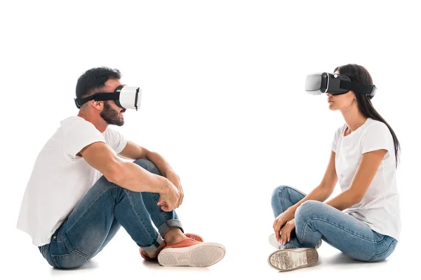 Seitenansicht eines glücklichen Mannes mit überkreuzten Beinen, der sitzt, während er Virtual-Reality-Headset in der Nähe von Frau auf Weiß verwendet — Stockfoto