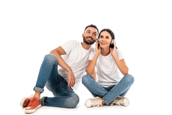 Mujer feliz escuchando música en auriculares cerca de hombre barbudo aislado en blanco - foto de stock