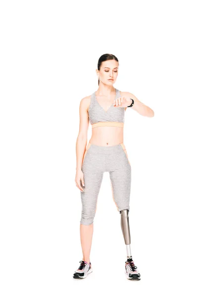 Ganzkörperansicht der Sportlerin mit Beinprothese beim Betrachten der Smartwatch isoliert auf Weiß — Stockfoto
