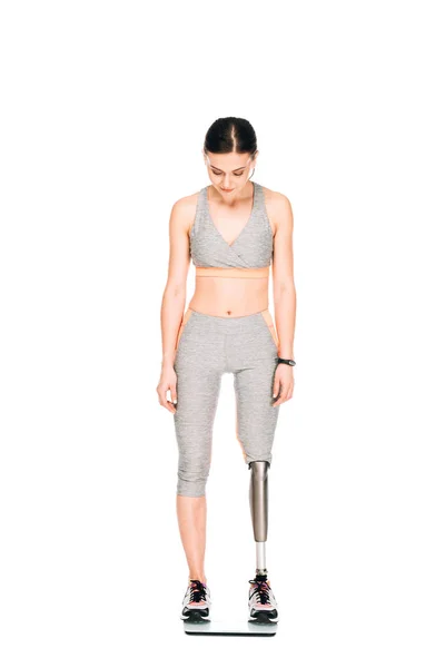 Full length view of disabled sportswoman with prosthetic leg on weighing scale isolated on white — Stock Photo