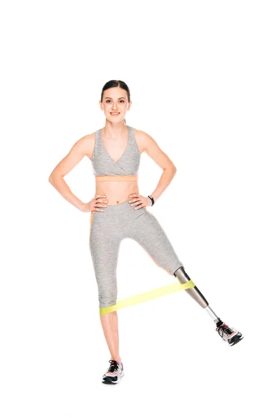 Full length view of smiling disabled sportswoman with prosthesis training with resistance band isolated on white — Stock Photo