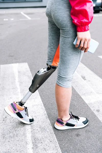 Частичный вид спортсменки-инвалида с протезом, держащей смартфон на улице — стоковое фото