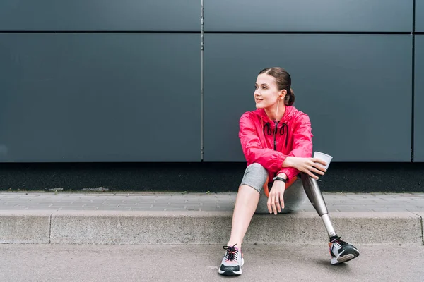 Спортсменка-инвалид слушает музыку в наушниках и держит кубок на улице — стоковое фото