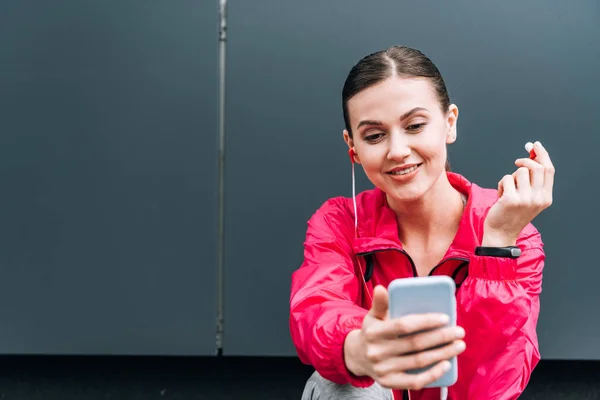 Smiling sportswoman in earphones using smartphone on street — Stock Photo