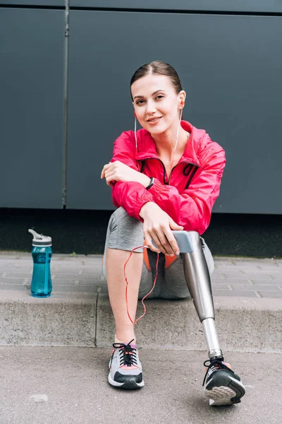 Улыбающаяся спортсменка-инвалид слушает музыку в наушниках на улице — стоковое фото