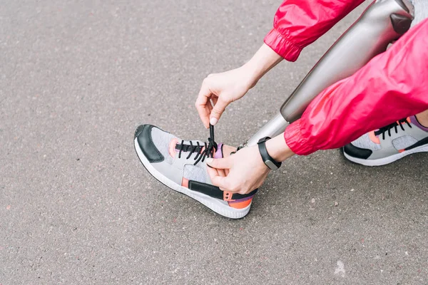 Cropped view of disabled sportswoman tying shoelace on street — Stock Photo