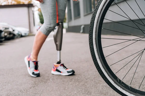 Partial view of disabled sportswoman with prosthesis and bicycle on street — Stock Photo