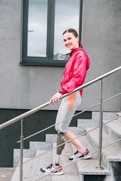 Vista completa de la sonriente deportista discapacitada con prótesis en las escaleras - foto de stock